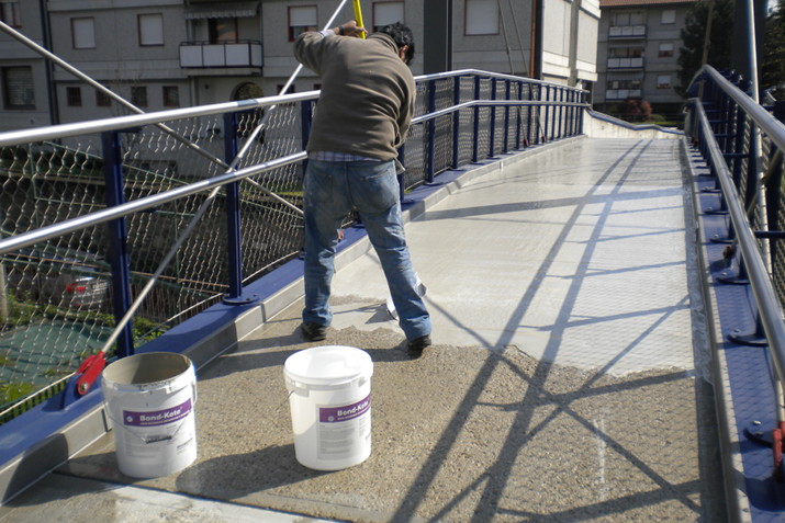 Foto di una passerella pedonale sospesa durante i lavori di rifacimento della superficie con Ercole
