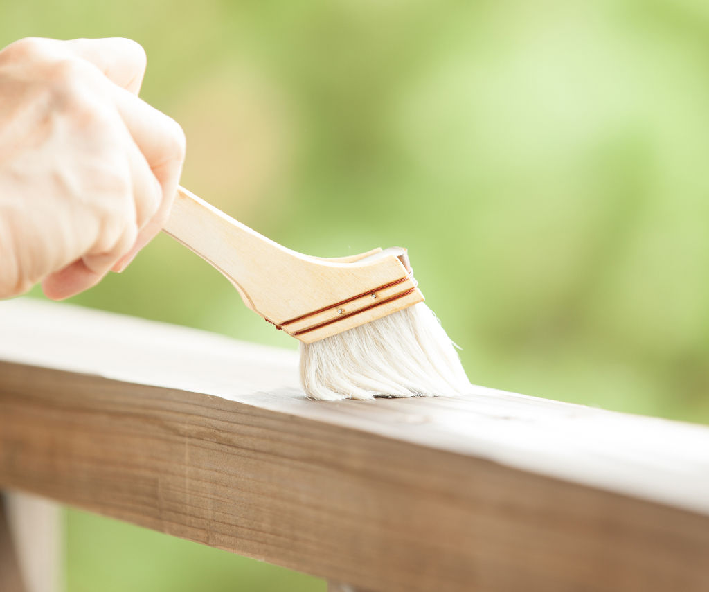 Applicazione a pennello di Everwood Bio Varnish su un elemento di recinzione in legno.